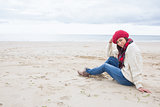 Smiling woman in stylish warm clothing sitting on beach