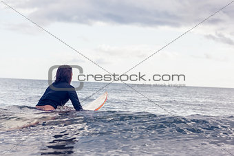 Rear view of a woman sitting on surfboard in water