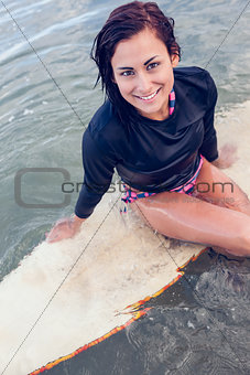 Portrait of a beautiful woman sitting on surfboard in water