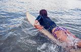 Rear view of a woman swimming over surfboard in water