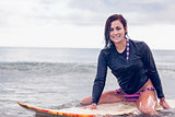 Beautiful young woman sitting on surfboard in water