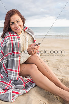 Woman covered with blanket using cellphone at beach