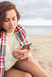 Woman covered with blanket using cellphone at beach