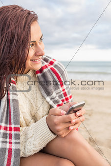 Woman covered in blanket with cellphone at beach