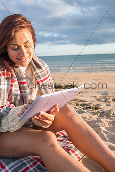 Woman covered with blanket using tablet PC at beach