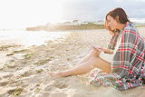 Woman covered with blanket using tablet PC at beach