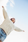 Woman in white sweater and denim shorts stretching her arms against sky