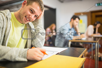 Smiling male student with others writing notes in classroom