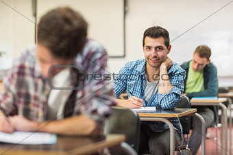 Male student with others writing notes in classroom