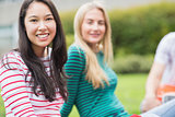 Smiling college student with blurred friend sitting in park