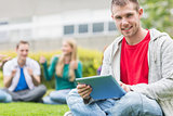 Smiling college boy holding tablet PC with students in park