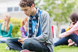 College boy using tablet PC with blurred students in park