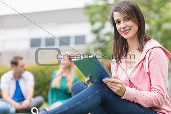 Smiling college girl using tablet PC with students in park