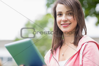 Smiling young college girl using tablet PC outdoors