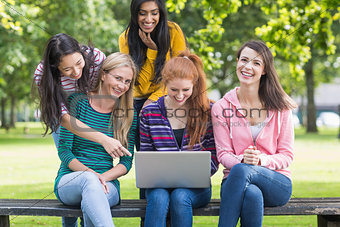 Cheerful college girls using laptop in park