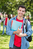 College boy holding books with blurred students in park