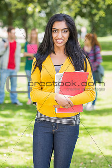 College girl holding books with blurred students in park