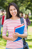 College girl holding books with blurred students in park