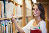 Smiling female student selecting book in the library