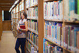 Female student standing against bookshelf in the library