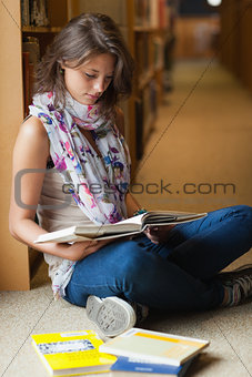 Female student reading a book in the library aisle
