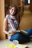 Smiling female student with books in the library aisle