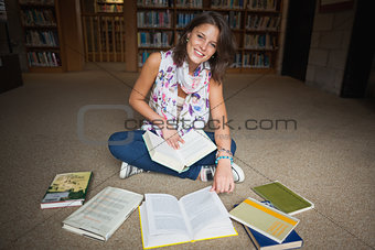 Smiling female student with books on the library floor