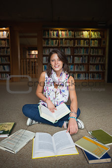 Smiling female student with books on the library floor