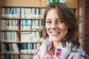 Smiling female student against bookshelf in library