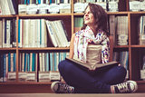 Thoughtful female student against bookshelf on the library floor