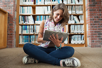 Female student against bookshelf using tablet PC on the library floor