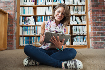 Happy student against bookshelf with tablet PC on the library floor