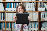 Female student against bookshelf holding out tablet PC in library