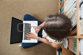 Student against bookshelf using laptop on the library floor