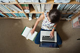 Student using laptop against bookshelf on the library floor
