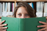 Female student holding book in front of her face in library