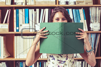 Student holding book in front of her face in library