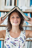Female student holding book over her head in library