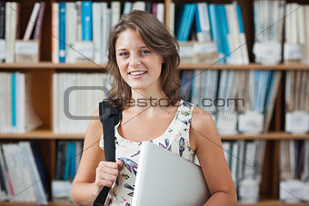 Female student against bookshelf with tablet PC and bag in library