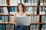 Female student against bookshelf using laptop in library