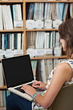 Side view of a female student against bookshelf using laptop in library