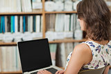 Female student against bookshelf using laptop in library