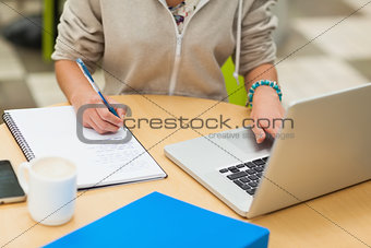 Mid section of a female student doing homework by laptop