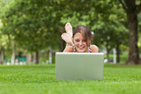 Woman lying on grass and using laptop at the park