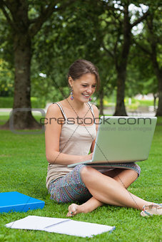 Smiling student using laptop with books at the park