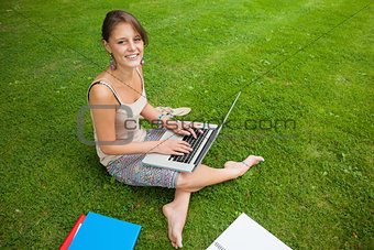 Student using laptop with books at the park