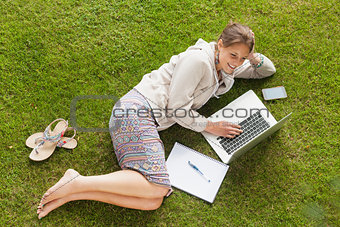 Female student using laptop with books at the park