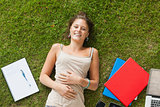 Smiling young woman lying on grass with books