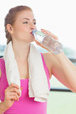 Woman with towel around neck drinking water in fitness studio