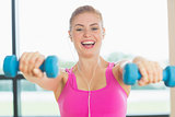 Cheerful woman exercising with dumbbells in fitness studio